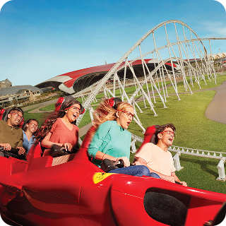 Group of people with safety goggles enjoying a ride in a red roller coaster on a sunny day.