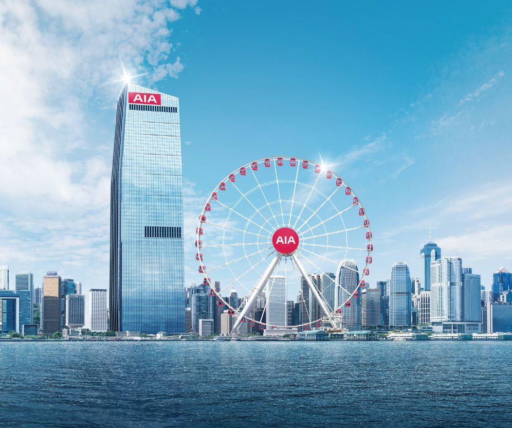 City skyline with a tall glass skyscraper and a large Ferris wheel, both branded with AIA logos, under a bright blue sky.