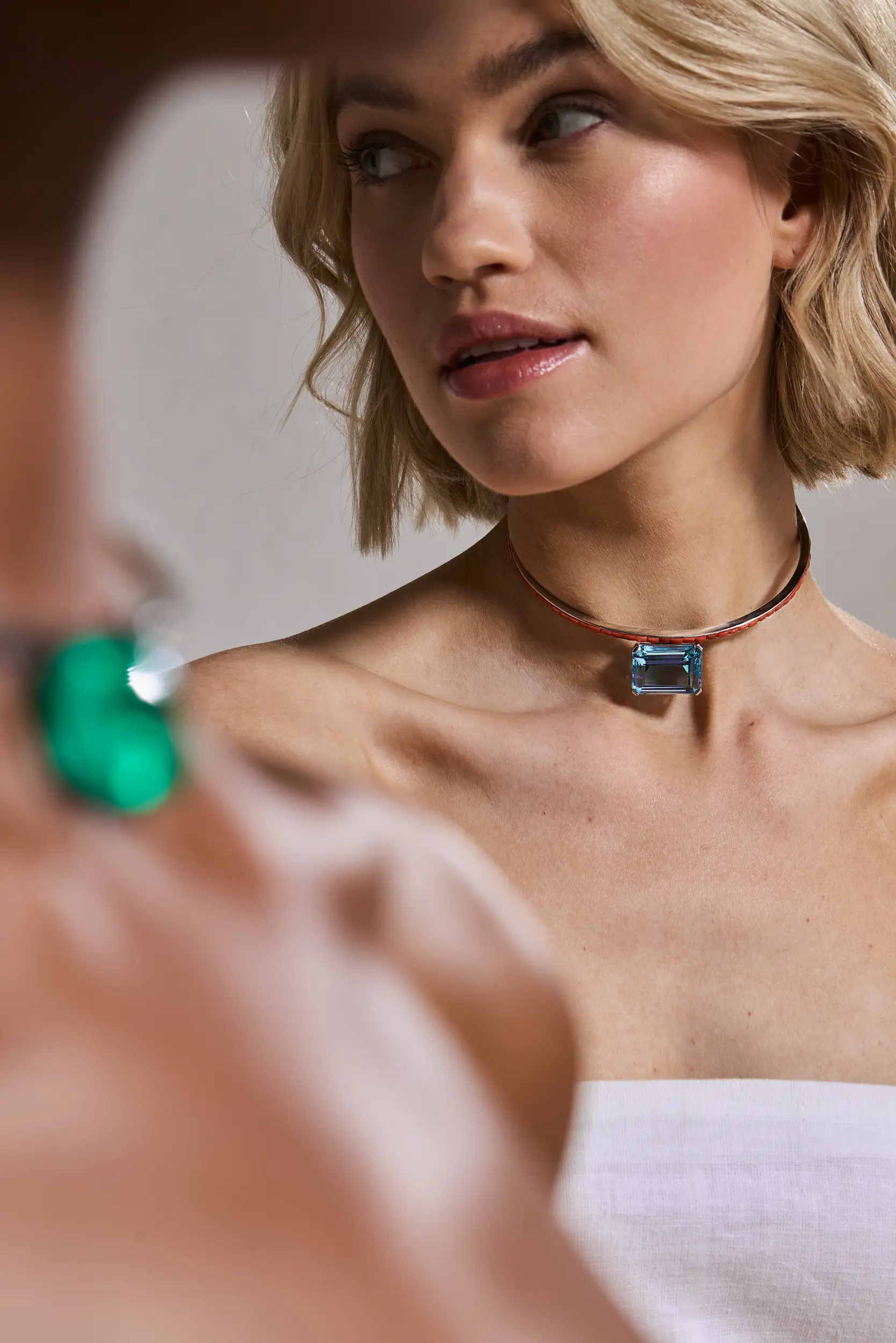 Close-up of a woman with short blonde hair wearing a choker necklace with a large rectangular blue gemstone, looking sideways.
