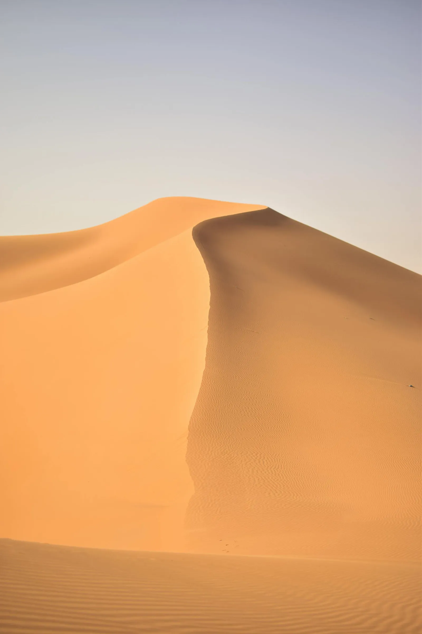 Large sand dune with a sharp crest under a clear sky.