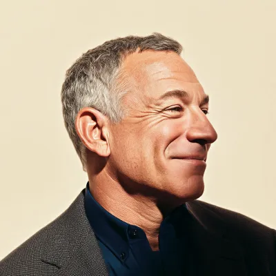Smiling middle-aged man with gray hair wearing a dark blazer and navy shirt against a beige background.