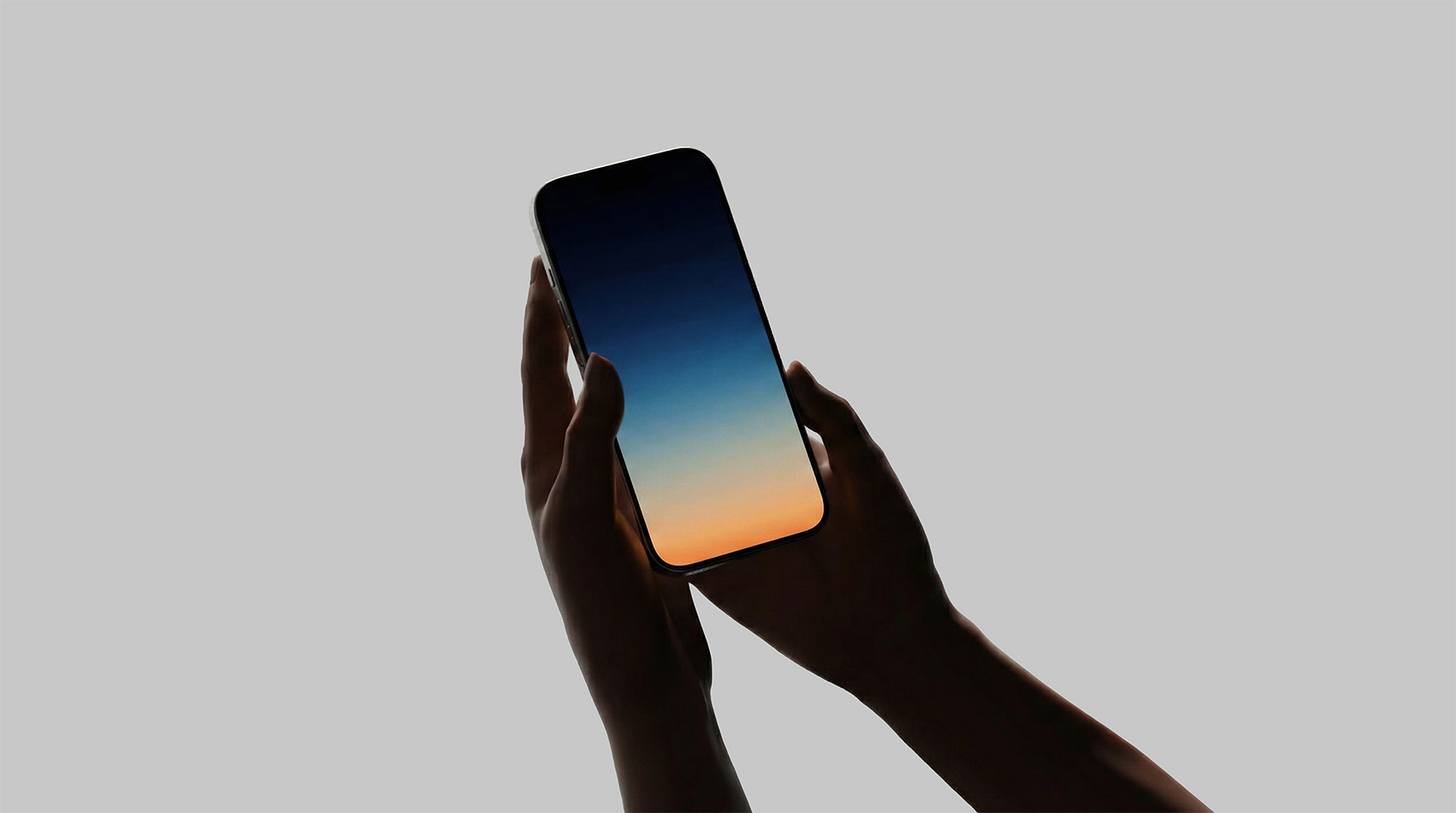 Hands holding a smartphone displaying a sunset gradient screen against a plain gray background.