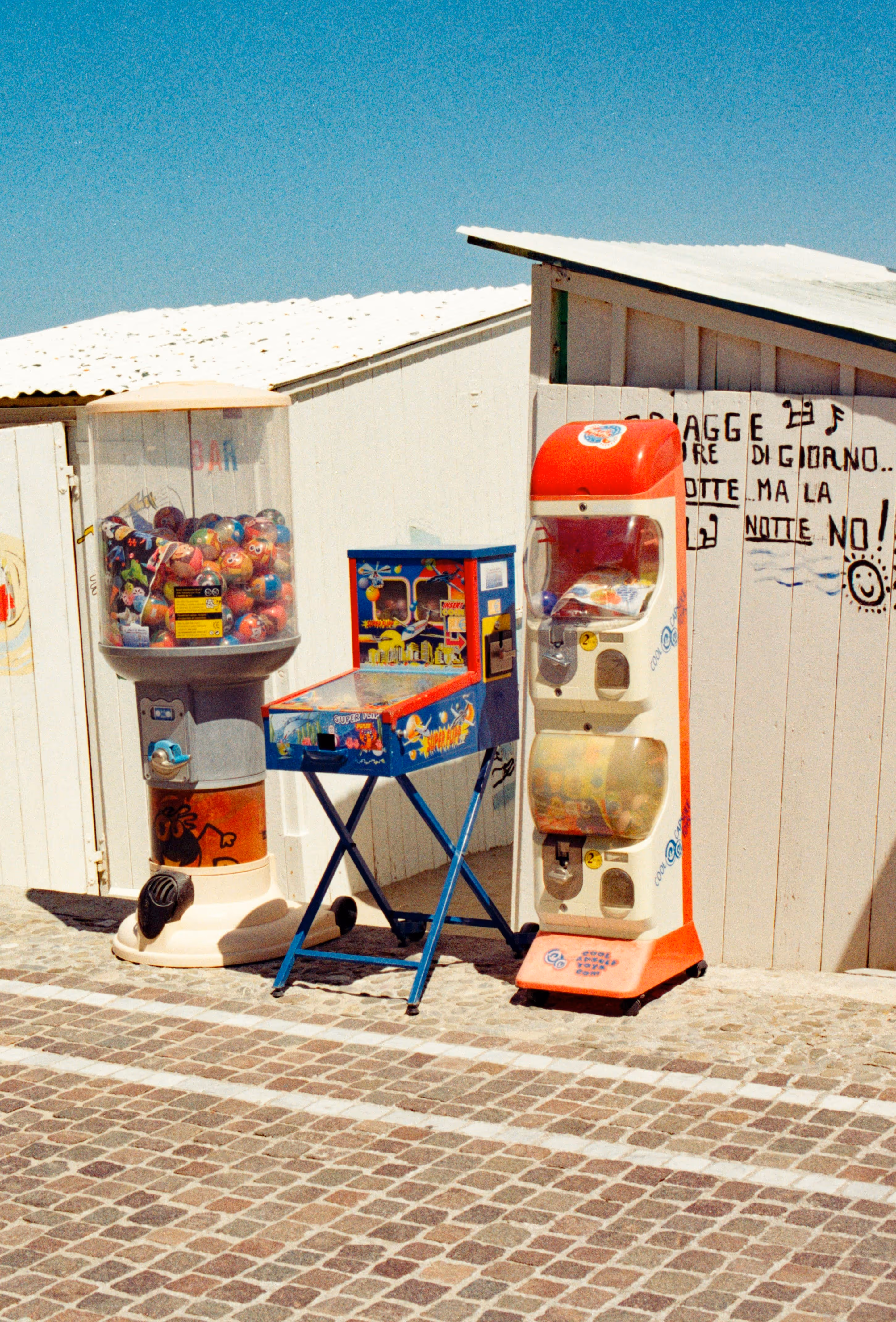 Bright seaside kiosk with vending machines on a cobblestone path.