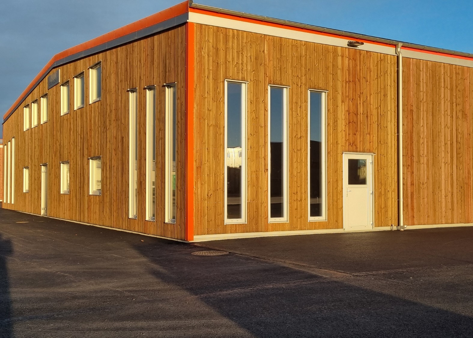 Modern träbyggnad med flera smala och rektangulära fönster och en vit dörr, inramad av en orange kant.