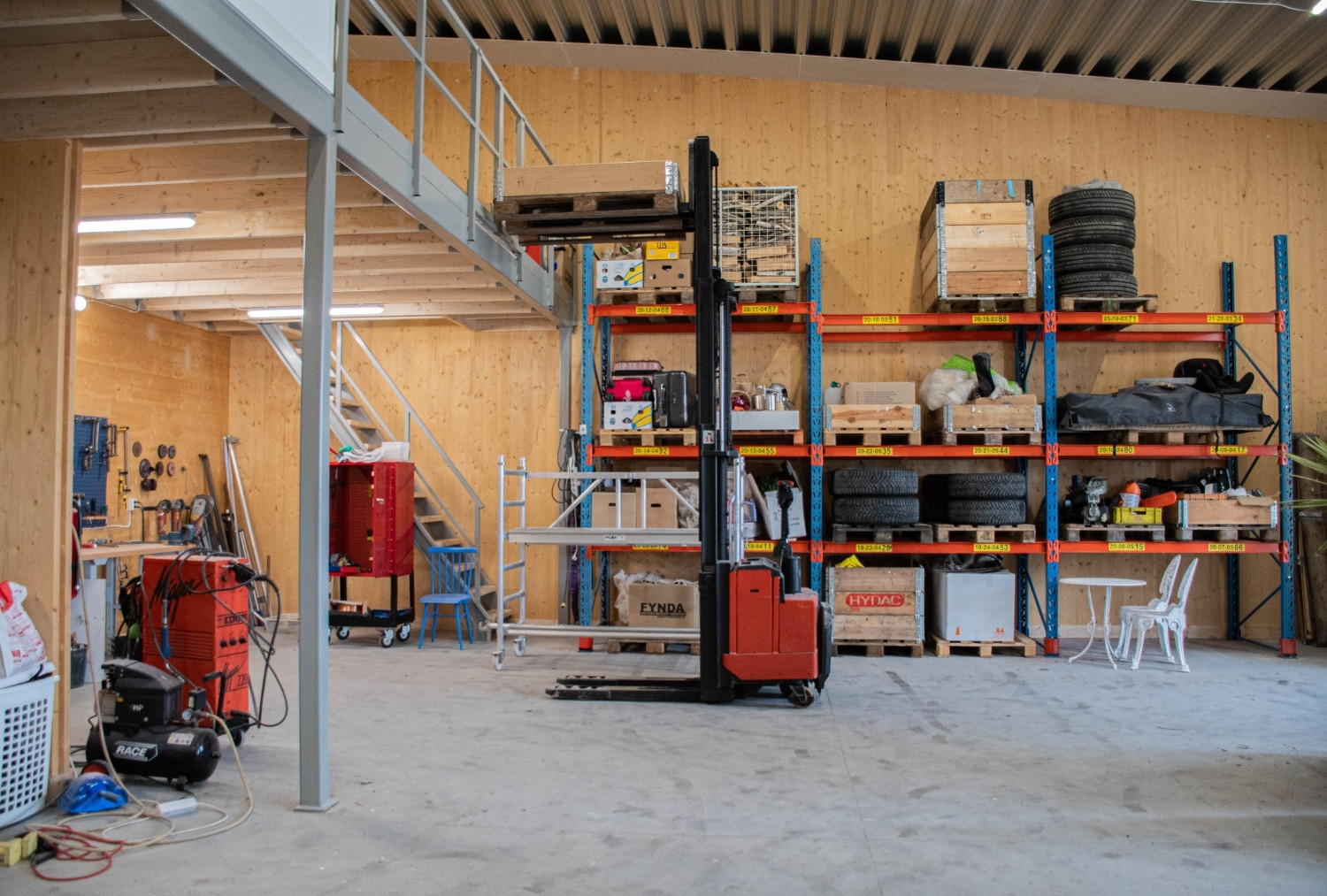 Lagerlokal med gaffeltruck framför hyllor fyllda med däck, träbruk och verktyg.