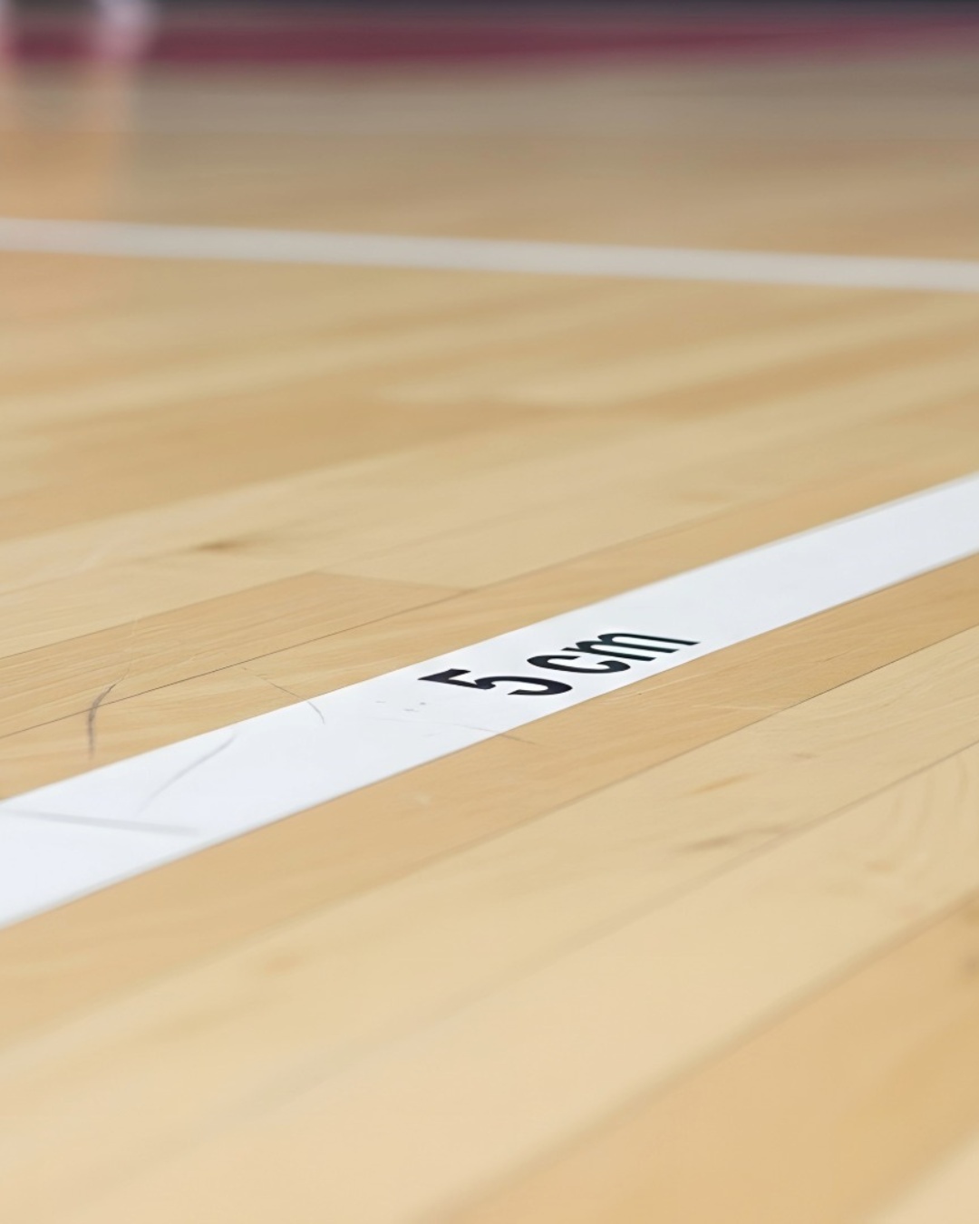 Närbild på en vit linje med texten '5 cm' på en ljus trägolvyta.