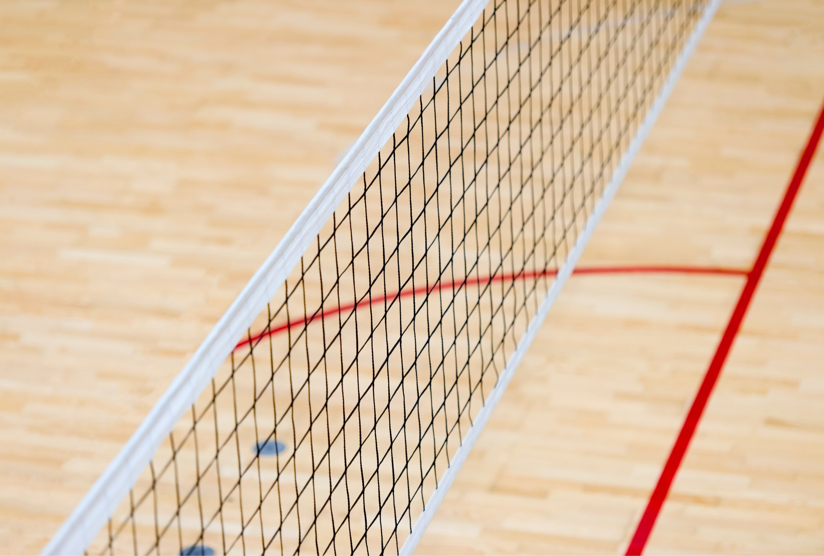 Volleybollnät över inomhusgolv med röda linjer på en sporthall.