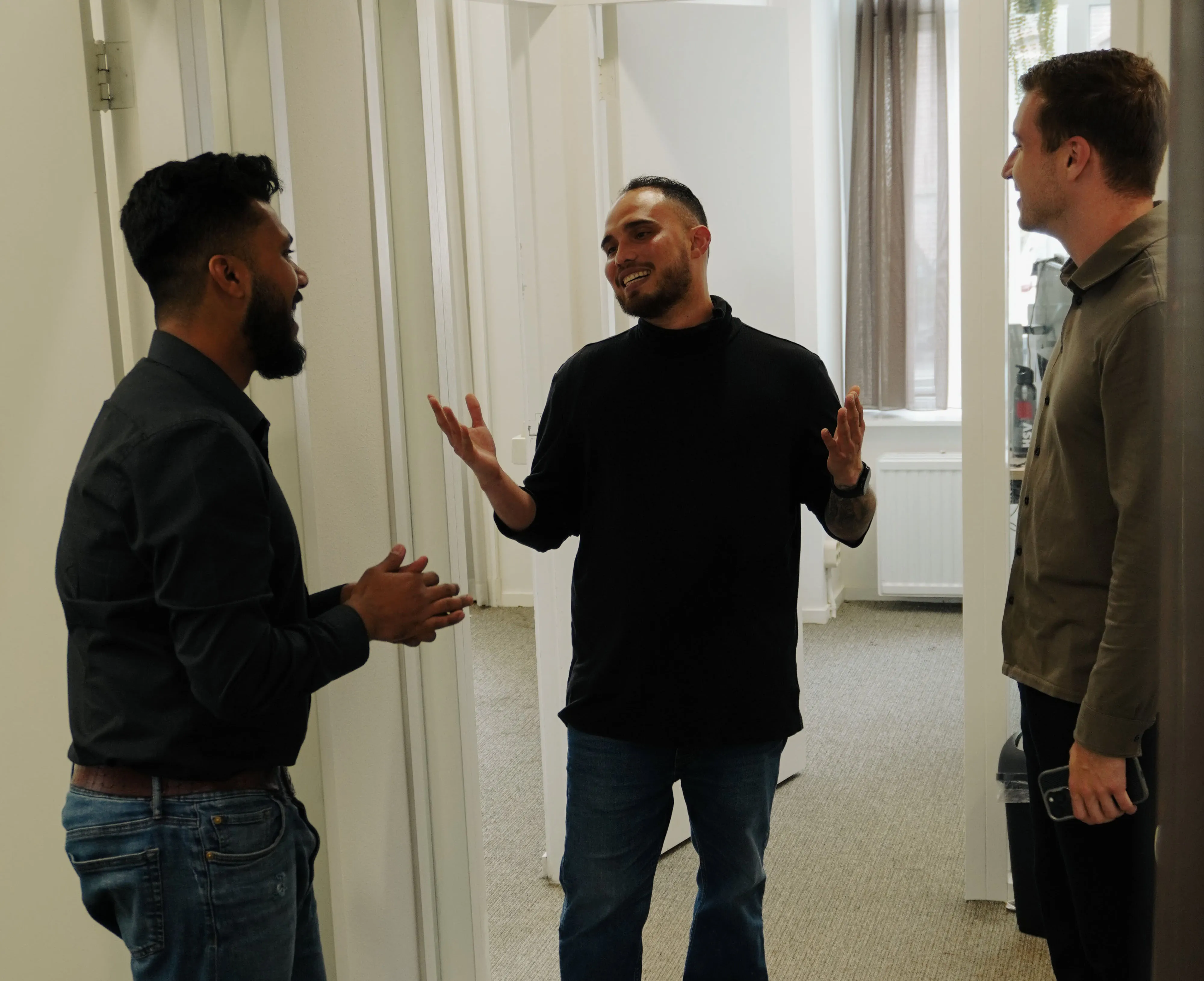 Three men standing and having a friendly conversation in an office hallway.