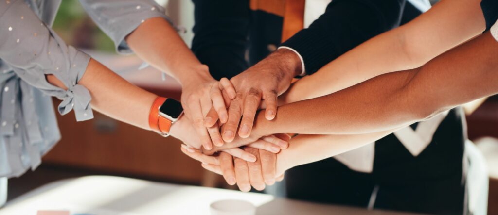 A photograph of a group of men and women's hands clasped together
