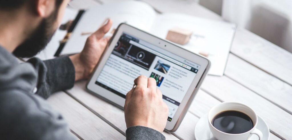 A photograph looking over the shoulder of a bearded man as he works on a tablet.