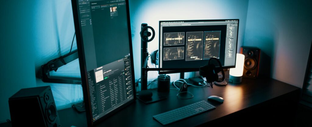 A photograph of a computer desk with dual monitors in a dark room. 
