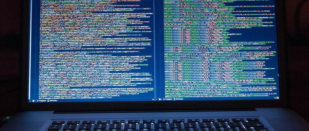 A photograph of a laptop computer. The screen displays lines of code.
