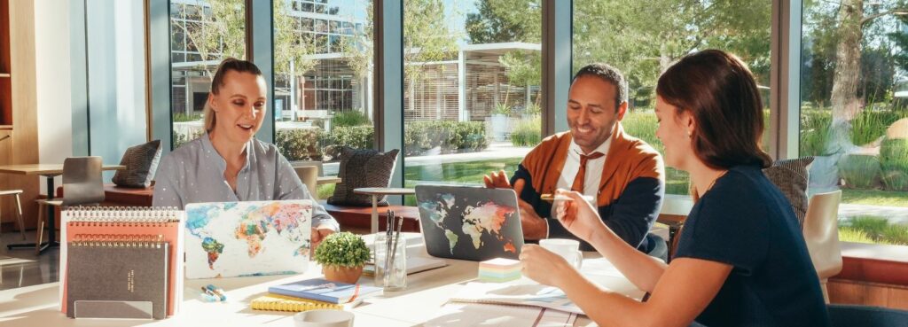 A photograph of two women and a man working on laptops together at a table.
