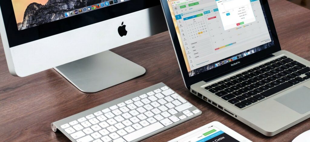 A photograph of a keyboard, laptop, monitor, and tablet next to each other on a desk.