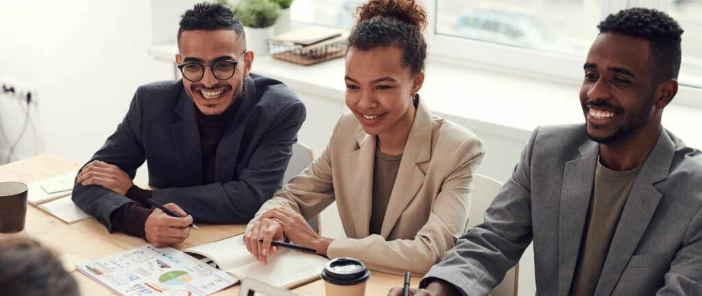 A photo of two men and a woman sitting at a desk and smiling at someone out of frame.