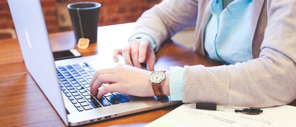 A close up photograph of a woman's hands as she types on a laptop.
