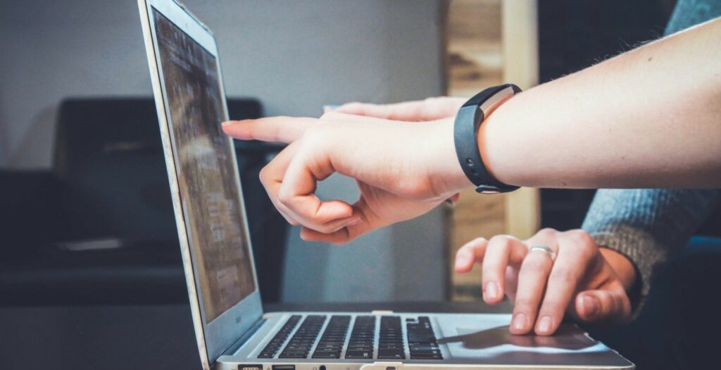 A photo of someone pointing at a laptop screen while someone else types.