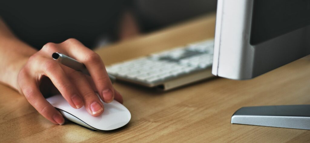 A photograph of a woman's hand as she uses a computer mouse on a wooden desk.