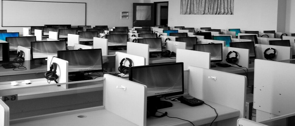 A ohotograph of a classroom with several cubicles holding computer monitors, keyboards, and headphones.
