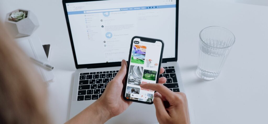 Someone is using their smartphone. Their open laptop is in the background of the photograph.