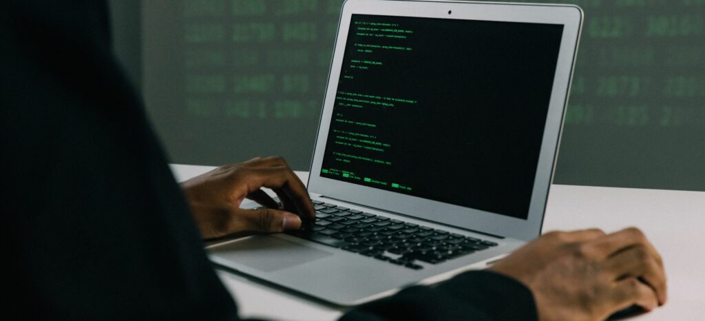 A photo of a man's hands as he types code on a laptop.