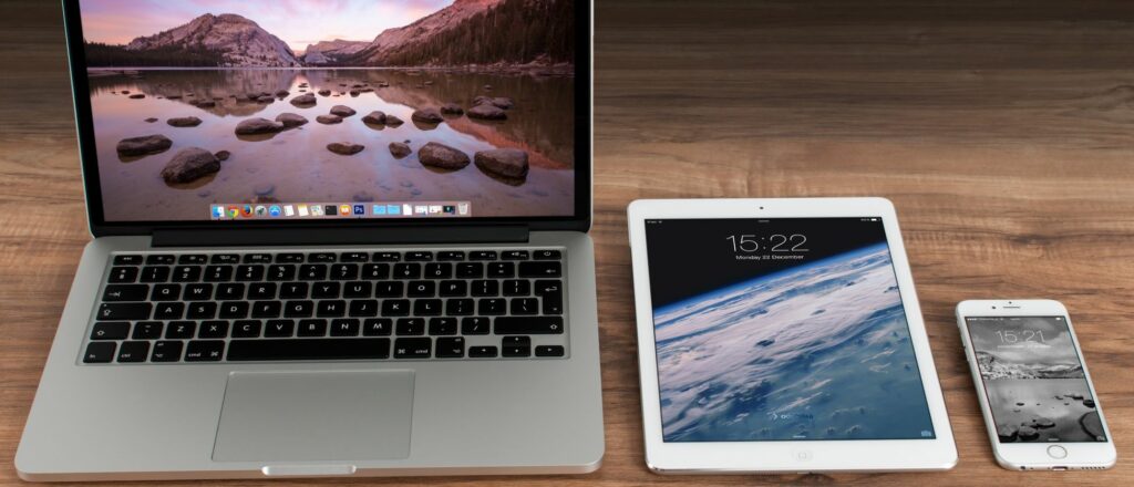 A photograph of a laptop, a tablet, and a smartphone on a desk.