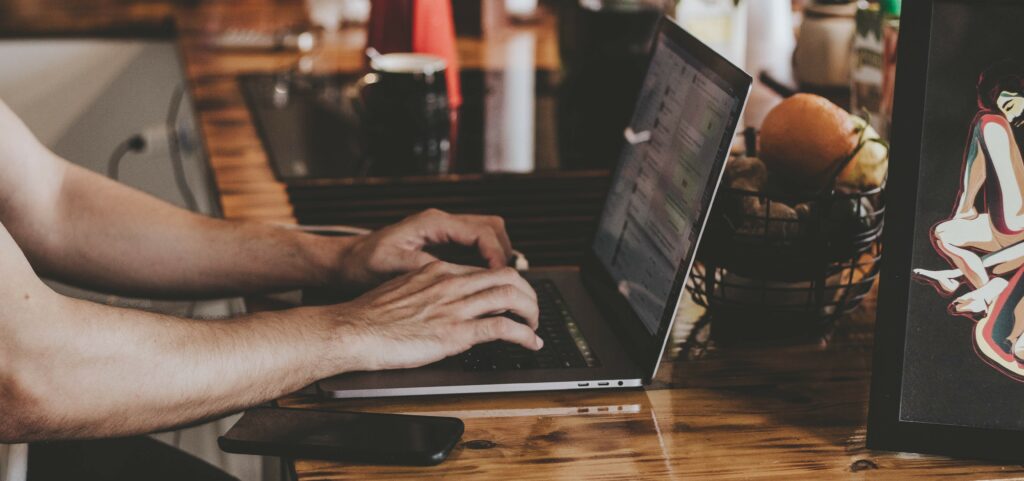 A man sits at a kitchen counter typing on a laptop