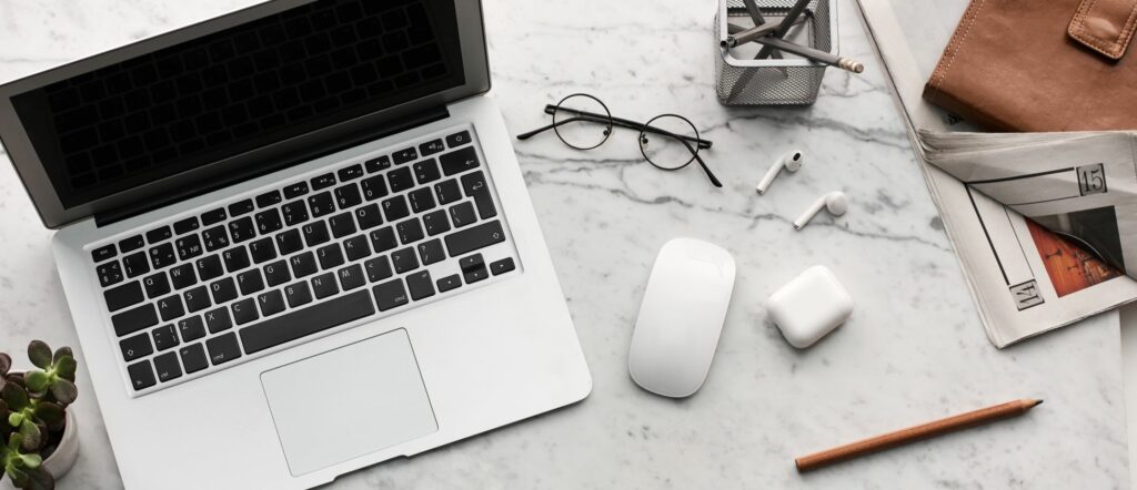 An overhead photo of a laptop on a white marble desk with various office supplies.