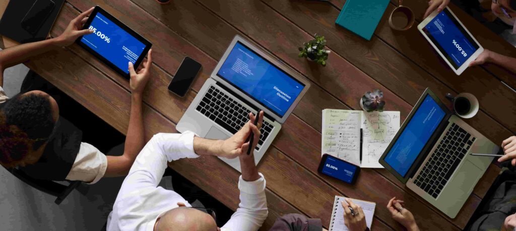 A group of people work on laptops, tables, and notebooks on a table.