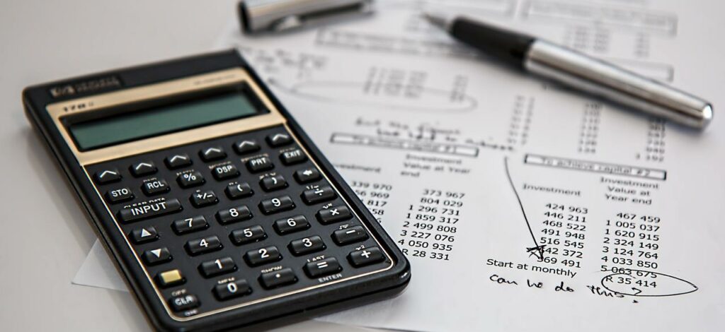 A photo of a calculator laid over a piece of paper. The paper has various finances and scribbled notes.