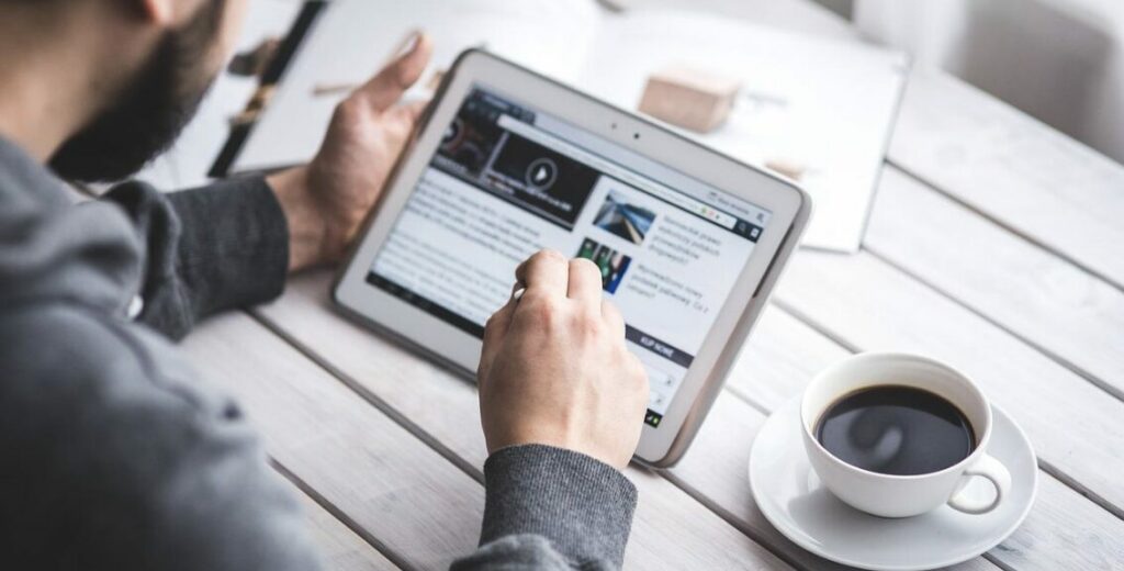A man works on a tablet while enjoying a cup of coffee