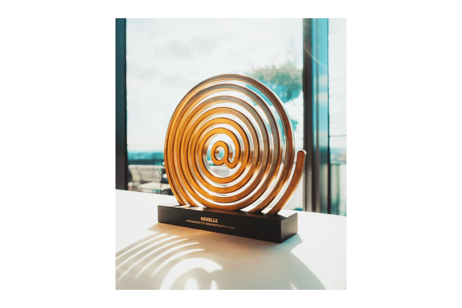 Goldener Spiral-Award auf schwarzem Podest im Sonnenlicht vor einer Fensterfront