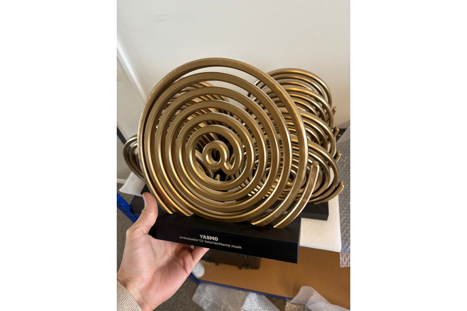 Spiral-Award mit gravierter Namensplatte in der Hand gehalten, weitere Awards im Hintergrund