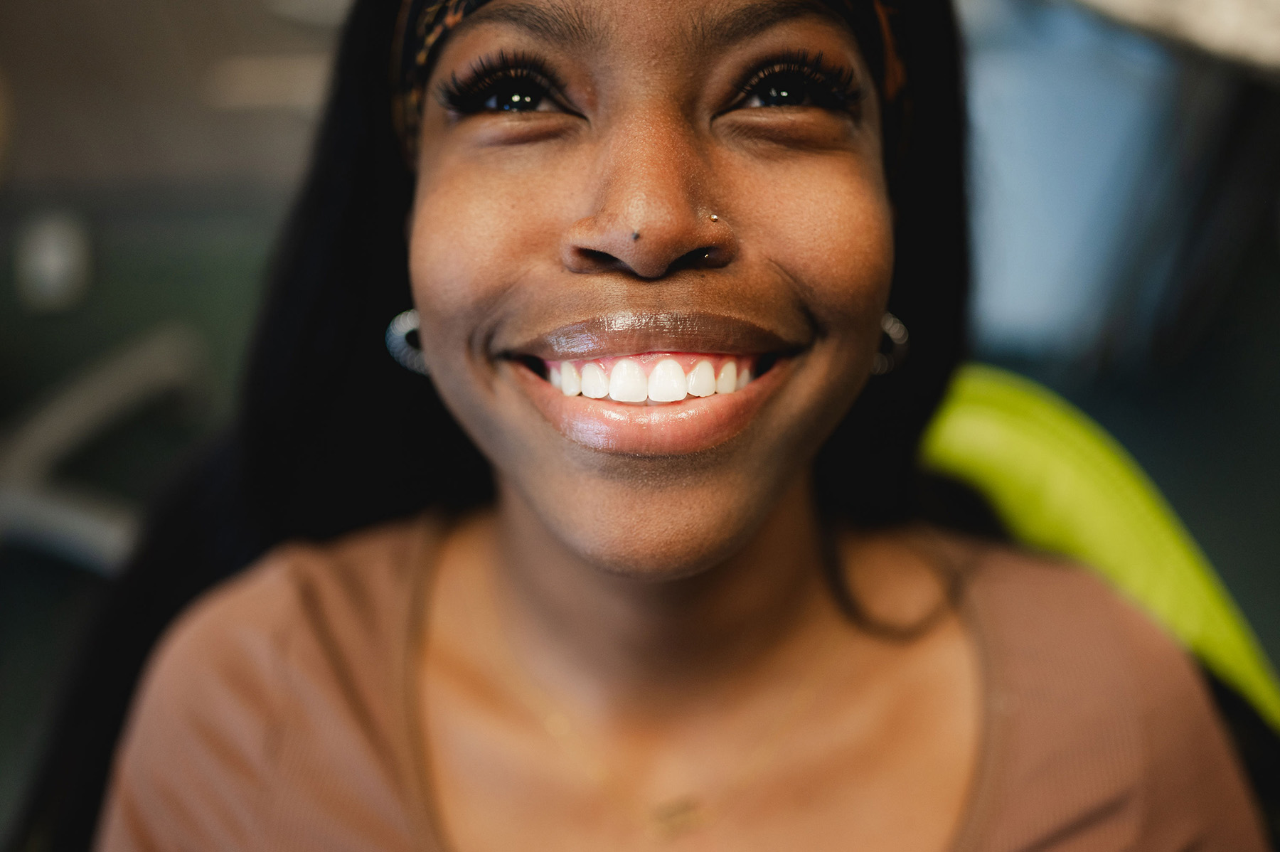 Close-up of a smiling woman with clear white teeth, wearing a headband and earrings.