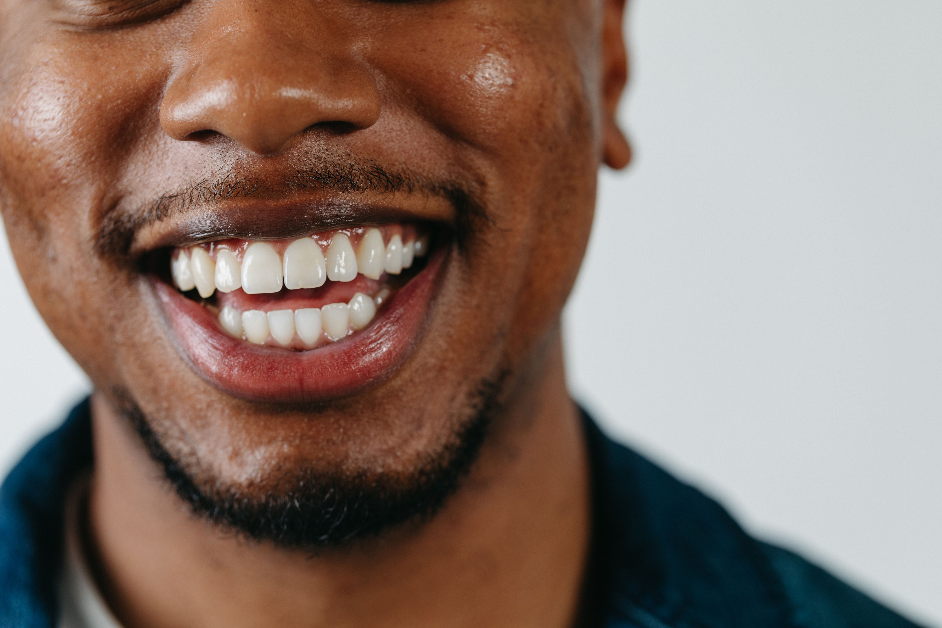 Close-up of a smiling man's mouth showing white teeth and a trimmed beard.