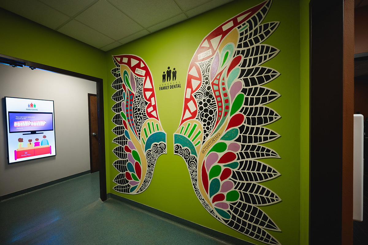 Colorful artistic wings mural on a green wall inside a dental office hallway with a sign reading Arkansas Family Dental.