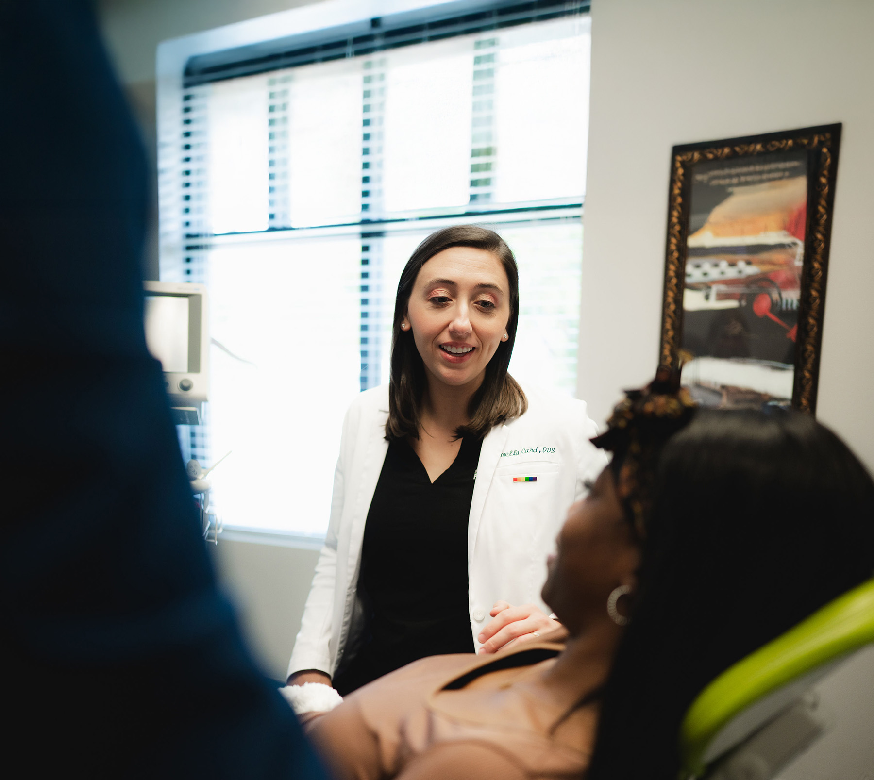 Female dentist in a white coat talking to a female patient reclining in a dental chair.
