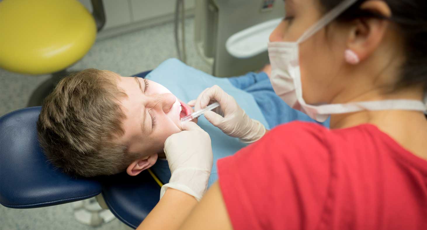 A female technician gives a novacaine shot to a sedated pediatric patient.