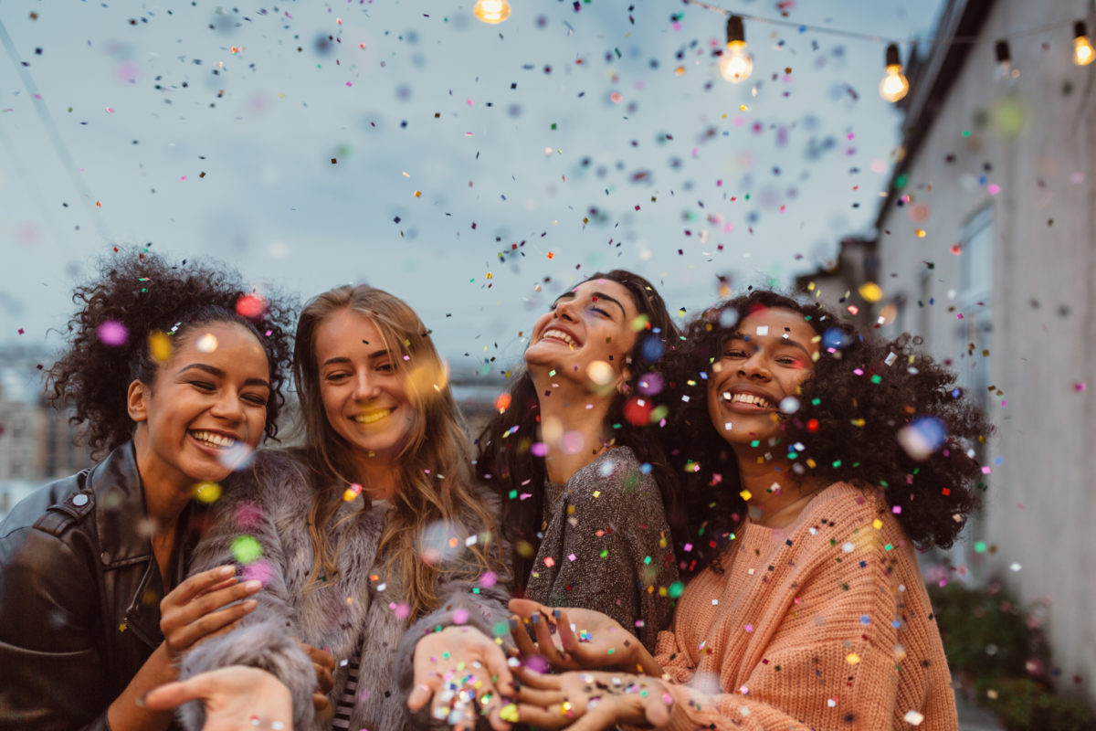 Four beautiful women celebrate with confetti and smile, displaying their perfectly, professionally whitened teeth.