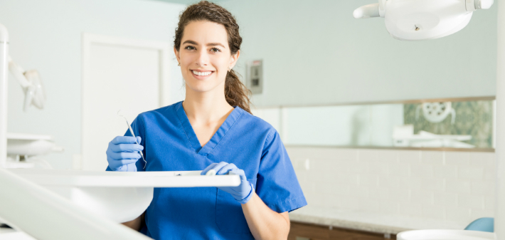 A Little Rock dentist qualified to perform Botox holds a dental scaler and smiles in a dental exam room.