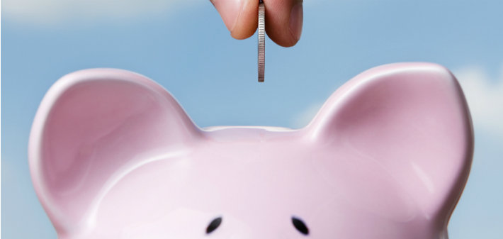 Two fingertips pinch a coin over the top half of a piggy bank.