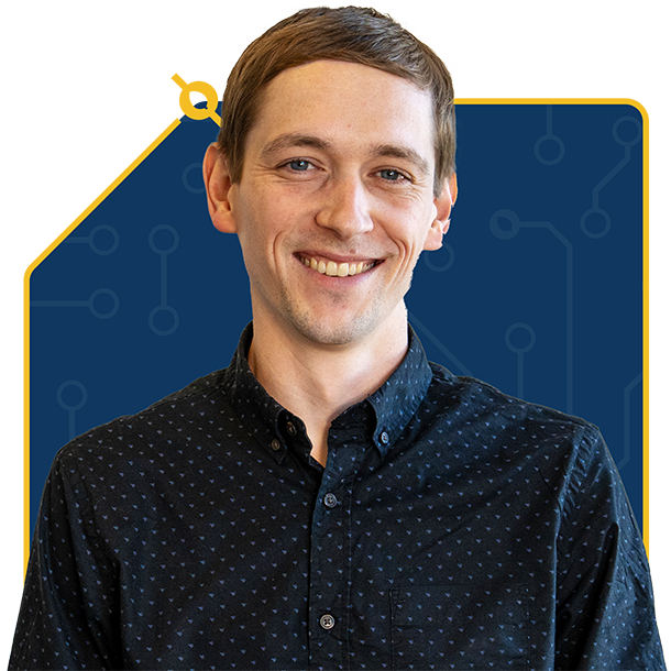 Smiling man with short brown hair wearing a dark blue patterned button-up shirt standing in front of a blue and yellow background with circuit-like design.