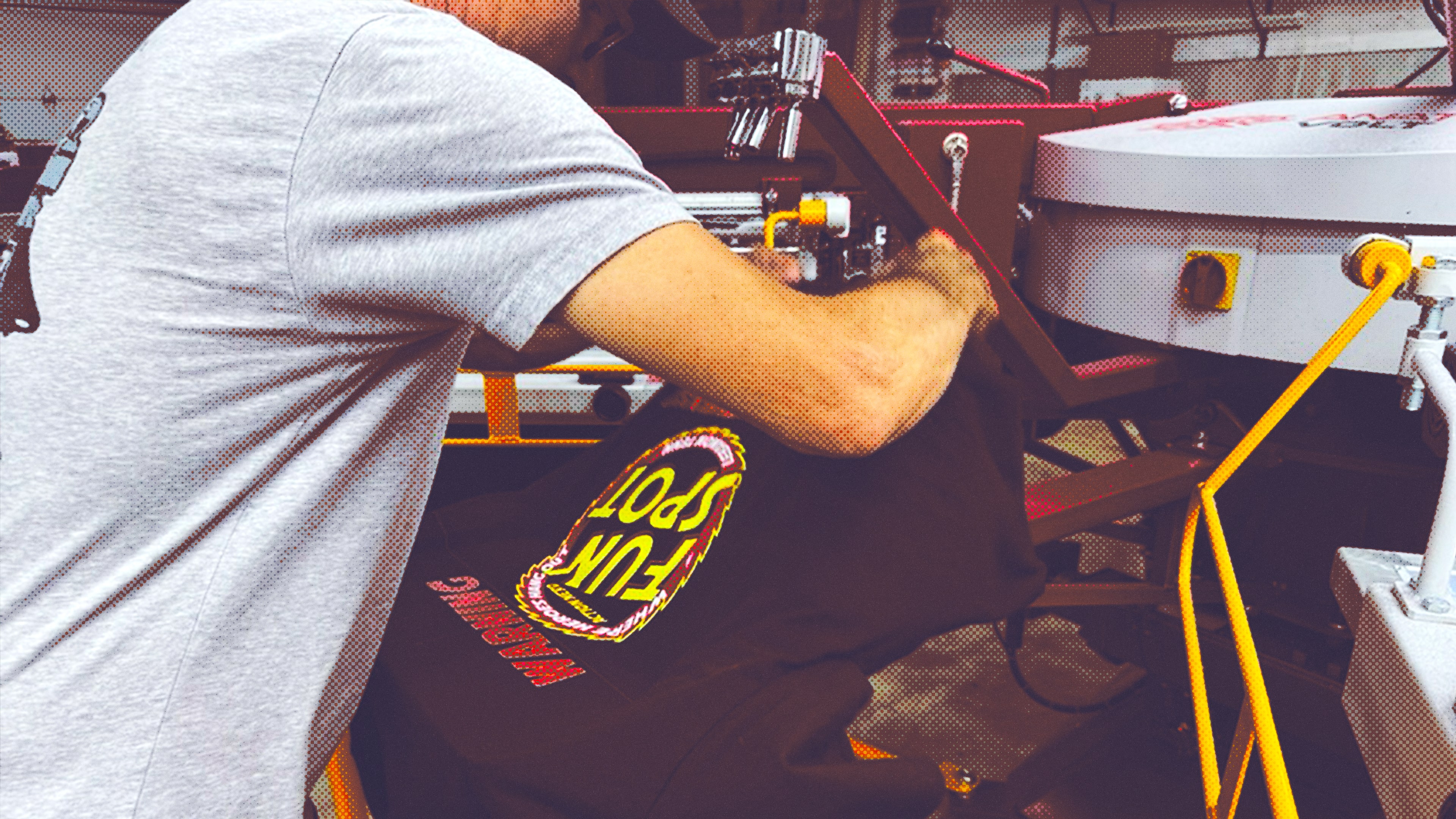 Person operating a screen printing machine applying a black garment with colorful text design.