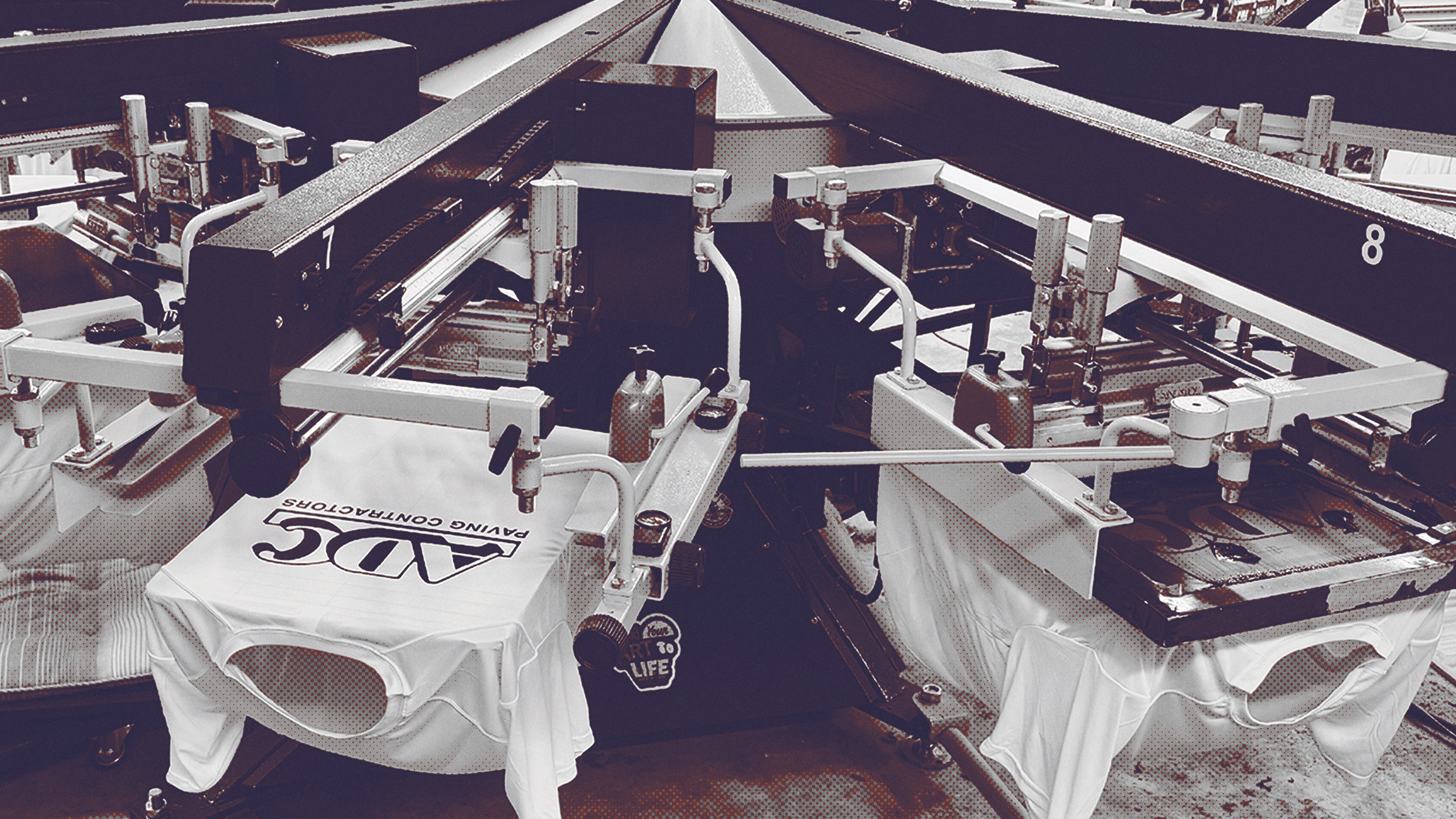 Screen printing machine printing logos on white t-shirts in a factory.
