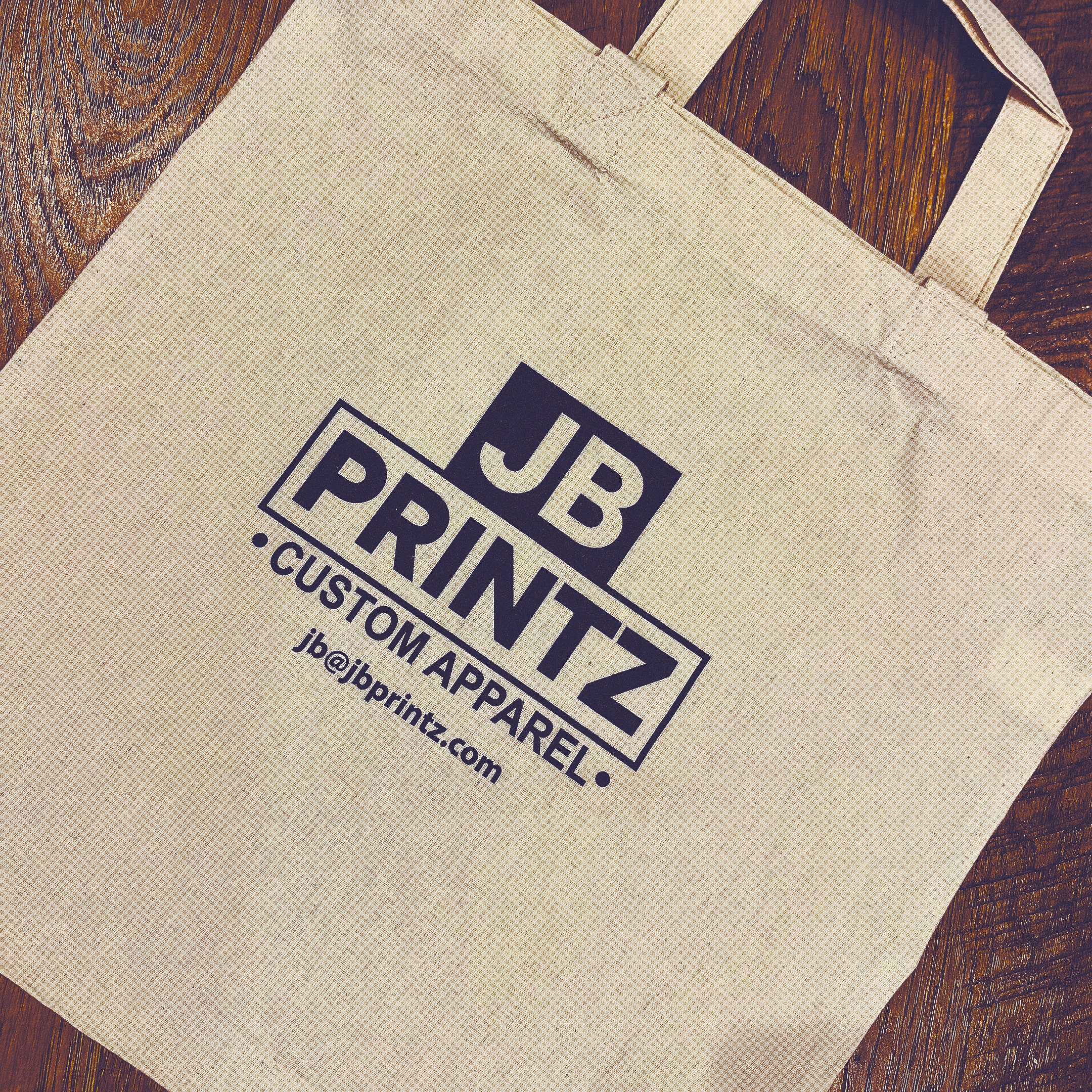 Beige fabric tote bag with JB PRINTZ Custom Apparel logo and email jb@jbprintz.com printed in black.