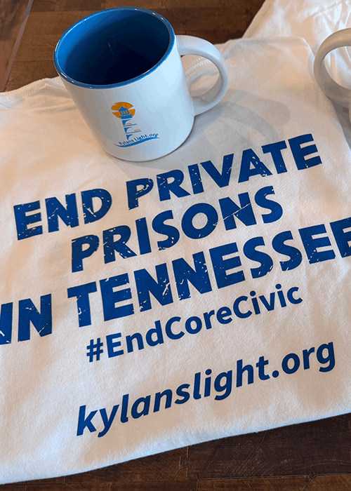 White t-shirt with blue text reading 'END PRIVATE PRISONS IN TENNESSEE #EndCoreCivic kylanslight.org' with a white mug featuring a blue interior and logo placed on top.