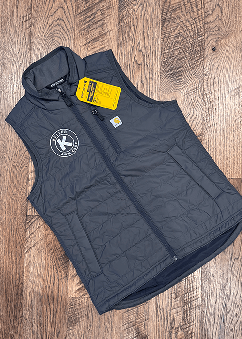 Black sleeveless insulated vest with Keller Lawn Care logo and Carhartt tag, laid flat on wooden floor.