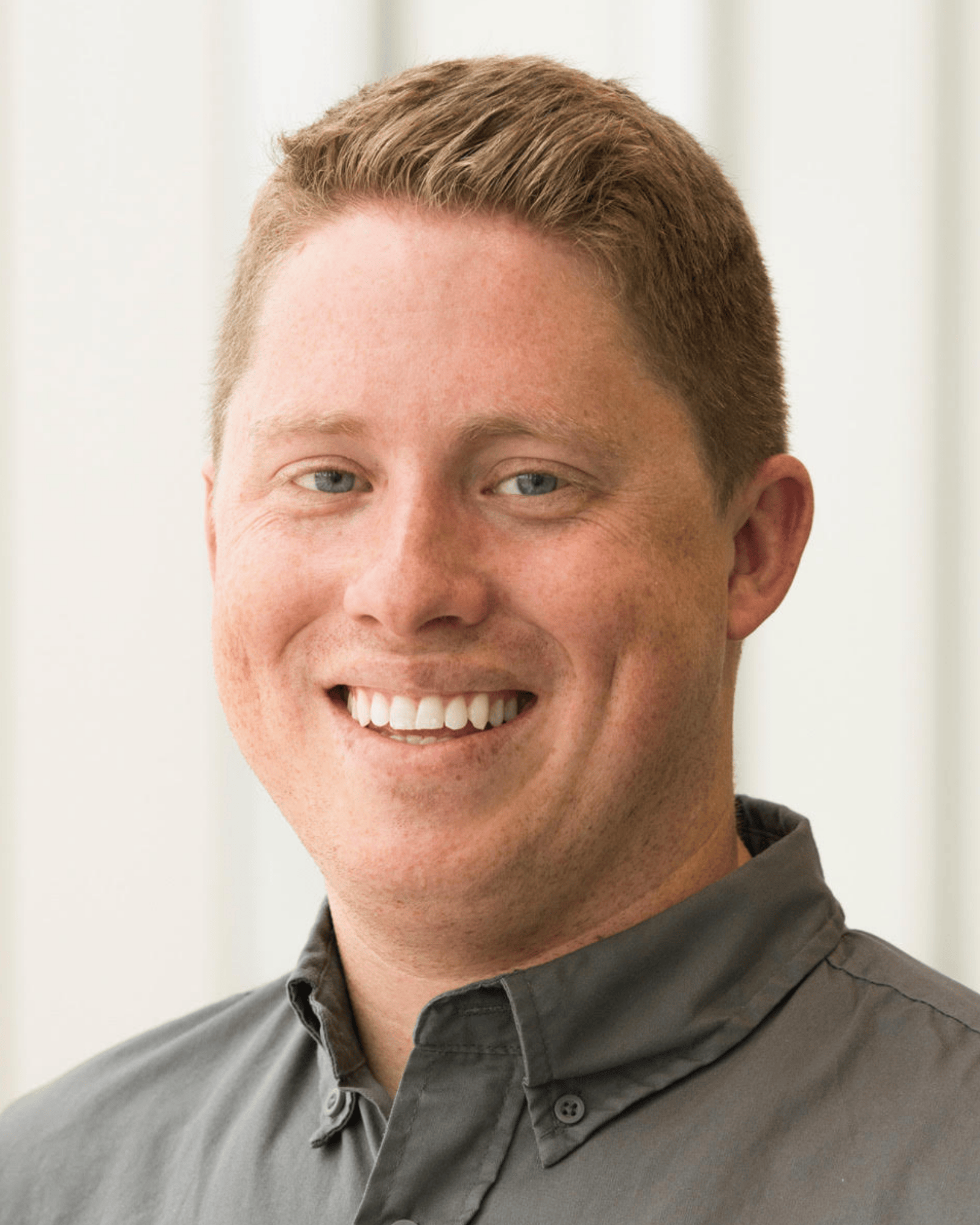 Smiling man with short light brown hair wearing a gray button-up shirt.