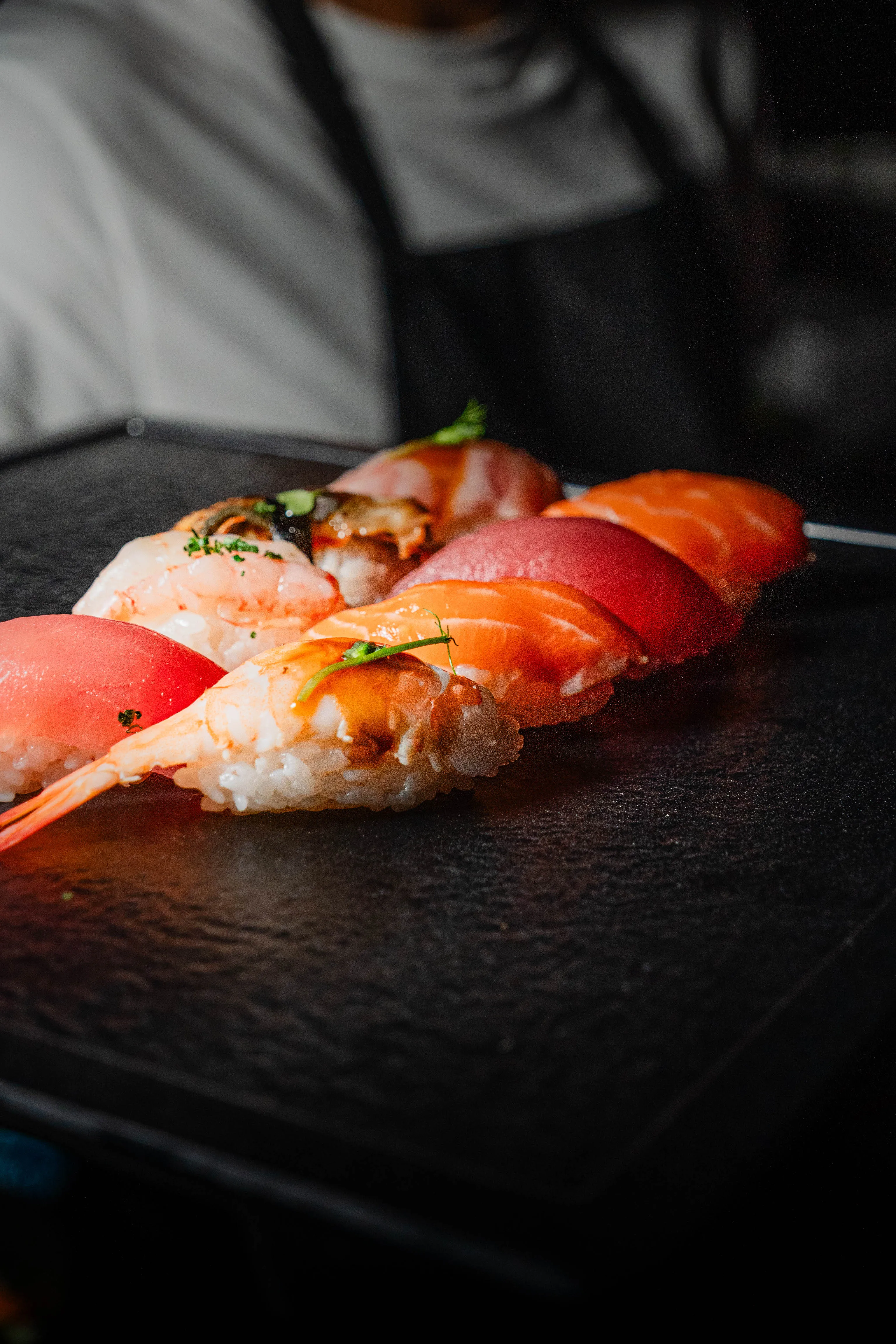 Verschiedene Sushi-Stücke mit Garnelen, Lachs und Thunfisch auf einem schwarzen Steinplatte.