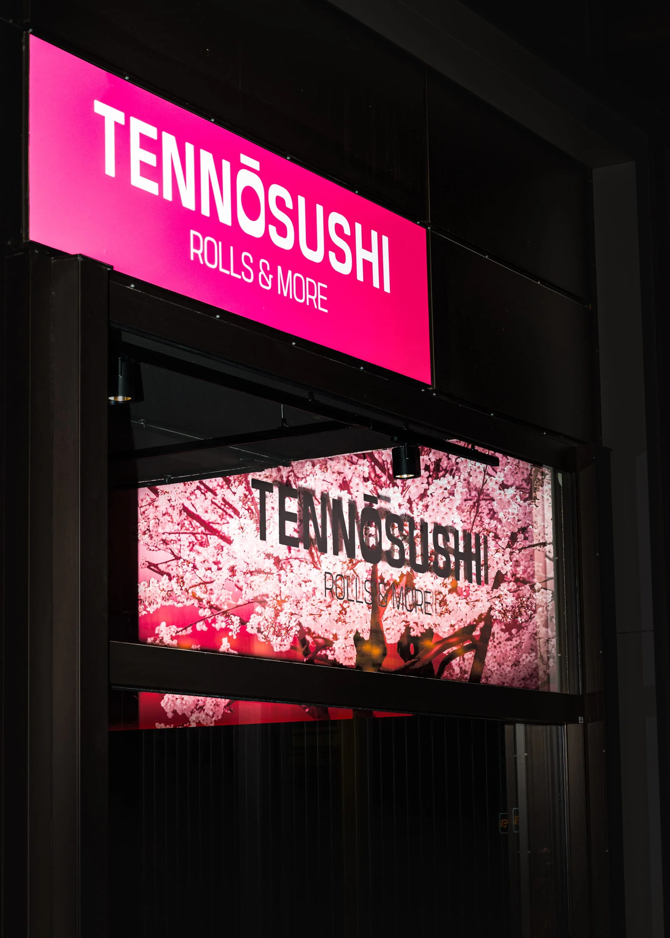 Leuchtschild von Tennōsushi Rolls & More über einem Fenster mit Kirschblüten-Dekor.